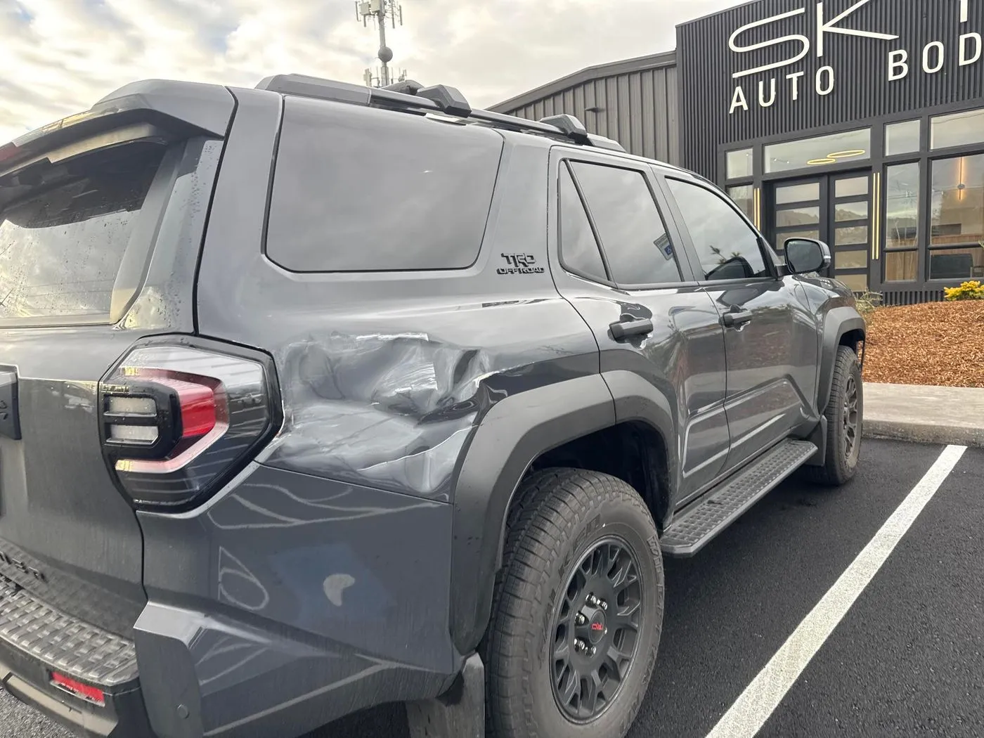 Gray Toyota 4Runner TRD Off-Road with a deep dent and creases in the rear quarter panel, parked outside Sky Auto Body in Medford, Oregon